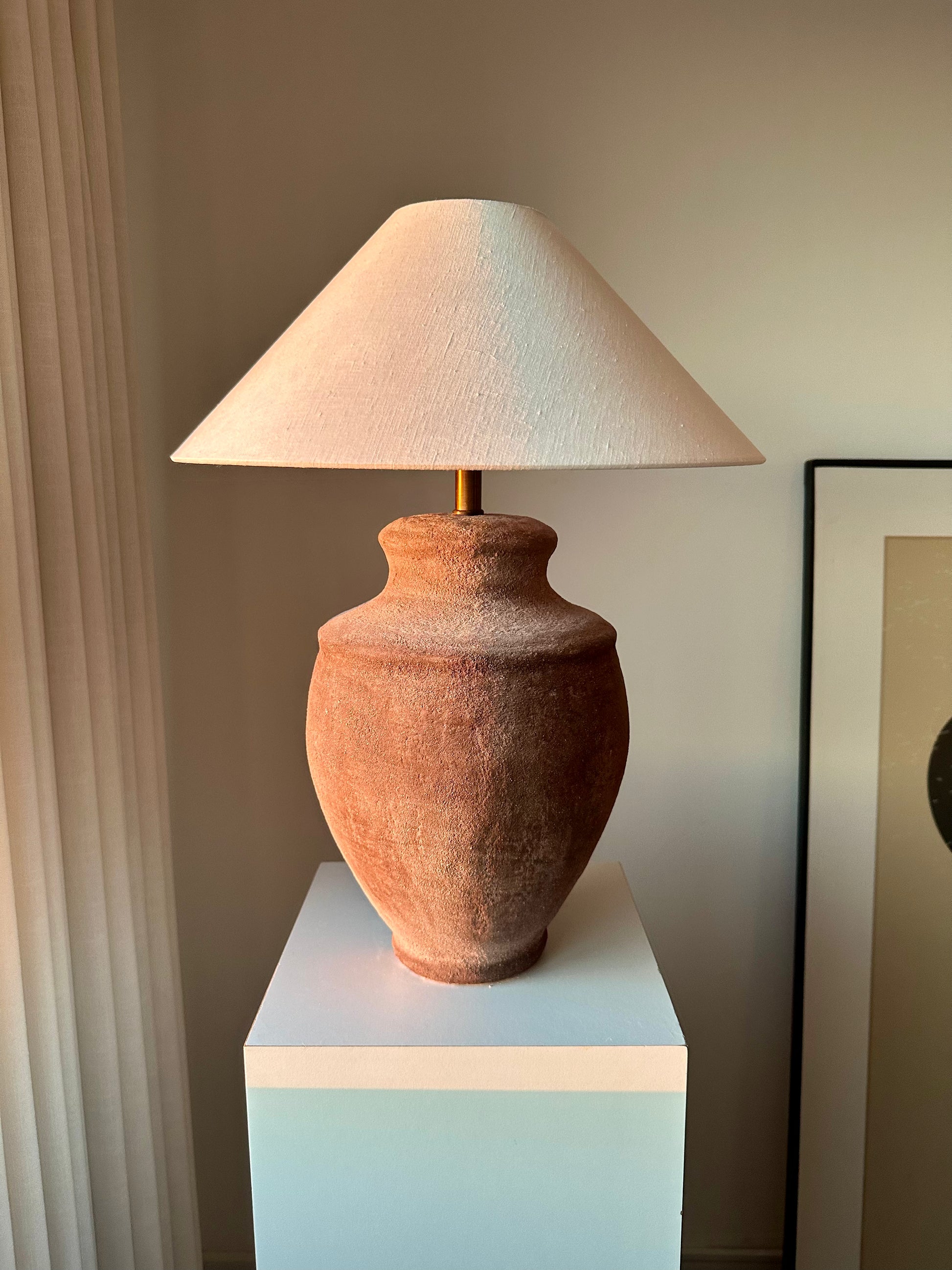 Devon earth tone ceramic table lamp with off-white linen lampshade on a white pedestal